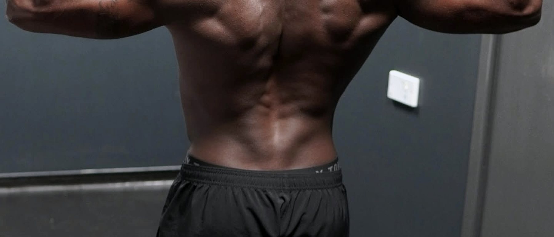Detail of a back double biceps pose showing olive wrist wraps